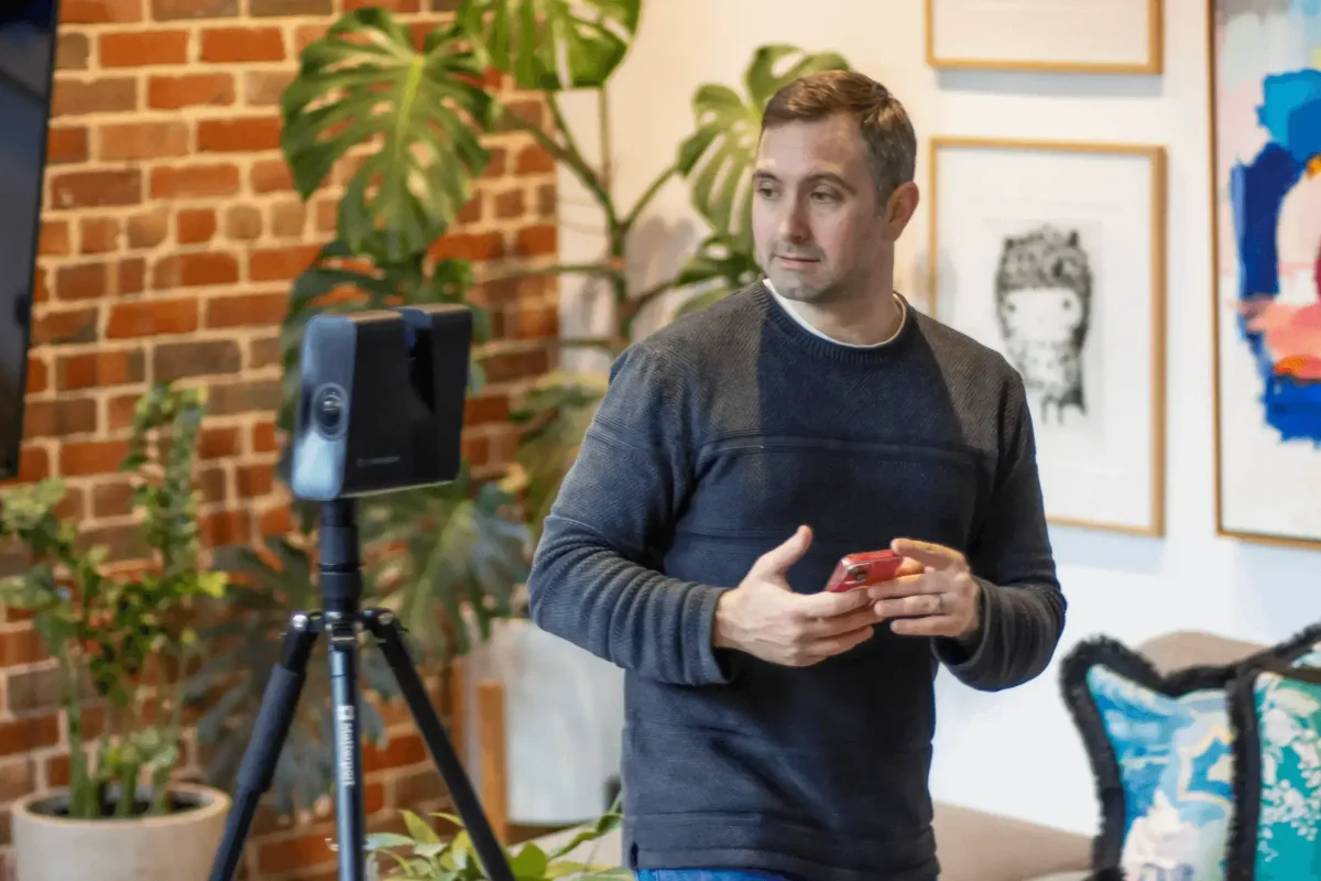 a man holding a phone looking in front of a Matterport Pro3 LiDAR Camera stand